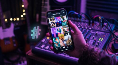 Mano sosteniendo un móvil con el feed de TikTok en un estudio de música, mejores hashtags para TikTok