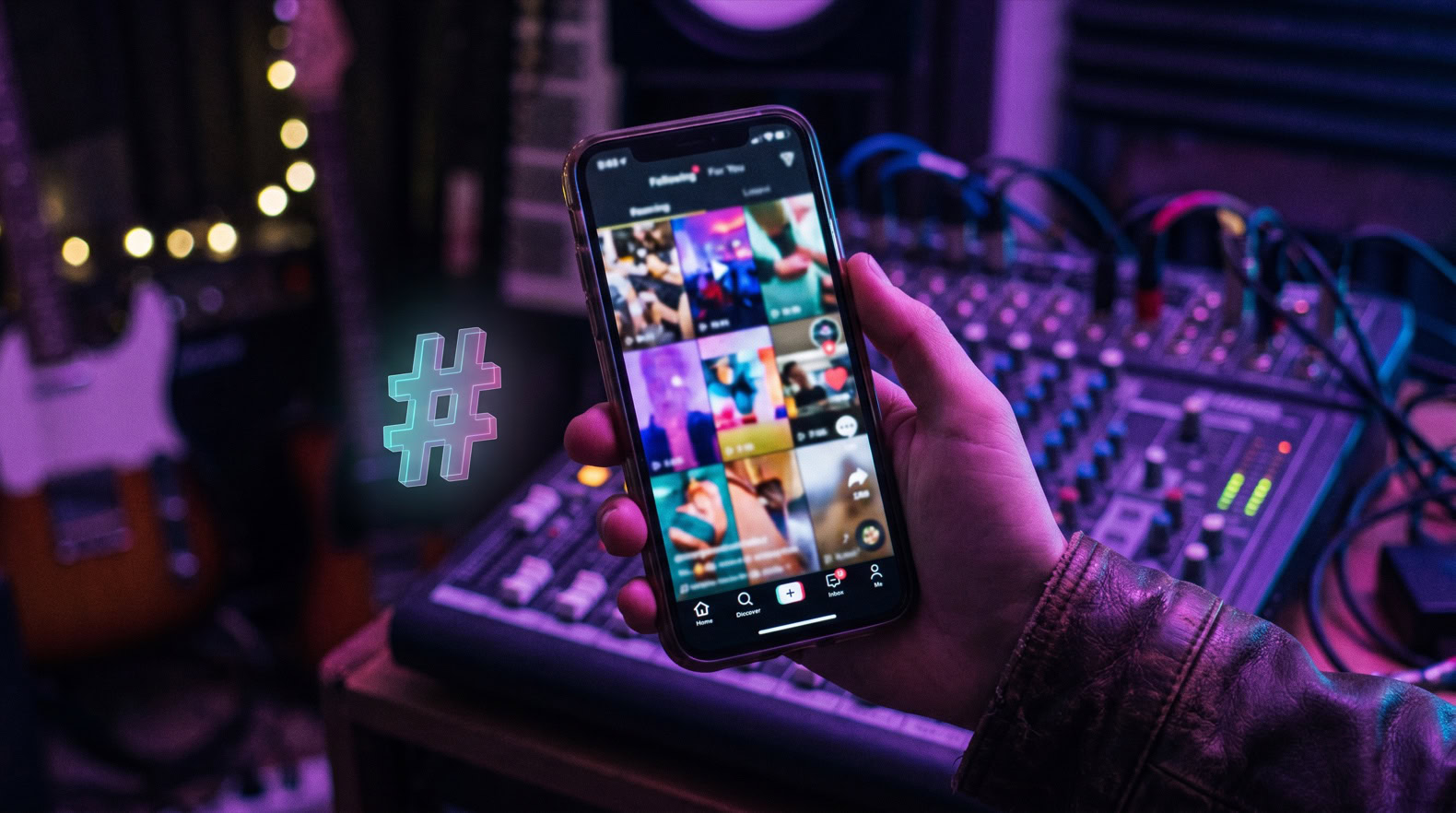 Mano sosteniendo un móvil con el feed de TikTok en un estudio de música, mejores hashtags para TikTok